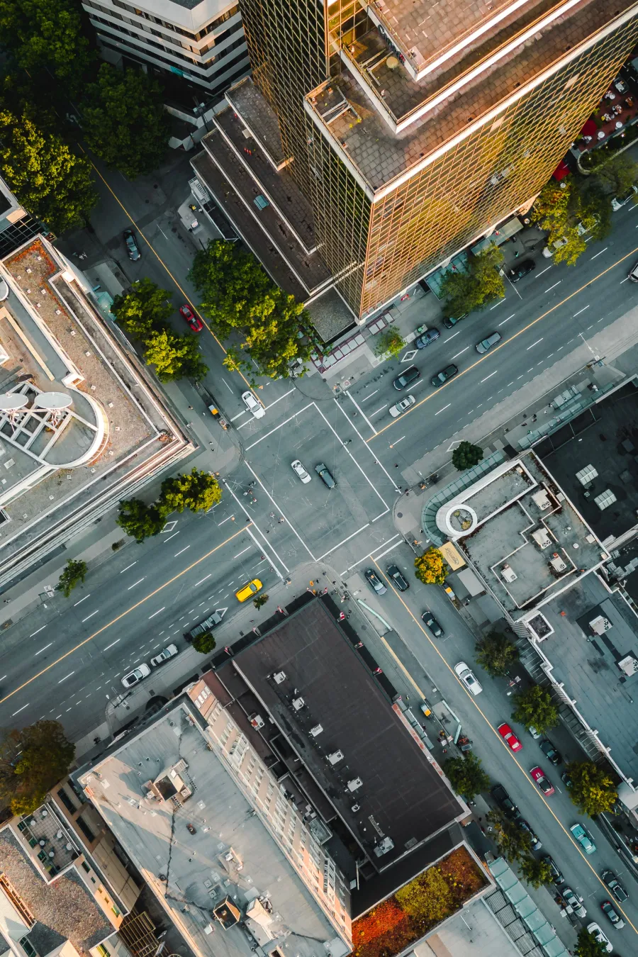 Aerial view of an urban intersection with traffic, trees, and tall buildings at sunset in a cityscape.