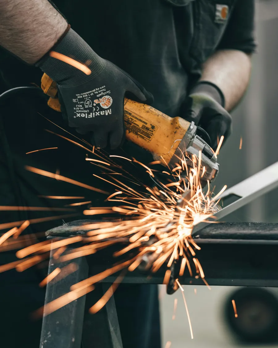Worker using a yellow angle grinder on metal creating bright sparks with protective gloves.