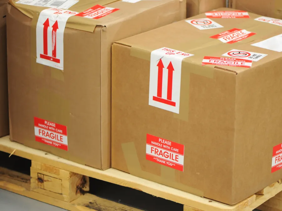 Cardboard boxes labeled fragile on wooden pallet ready for shipping or storage in warehouse