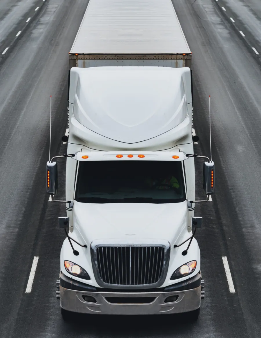 Front view of a white semi-truck driving on a multi-lane highway with headlights on
