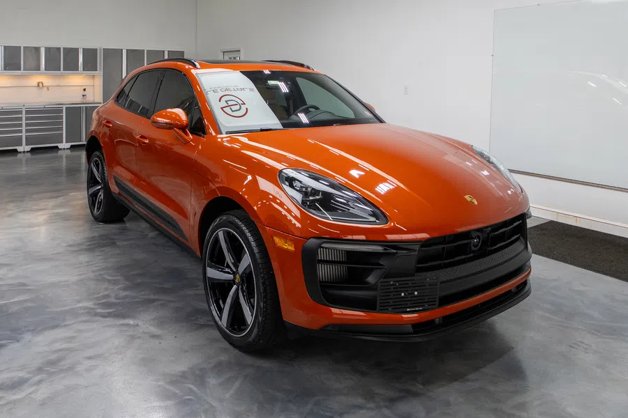 Orange Porsche SUV parked in a modern showroom with polished concrete floor and white walls.