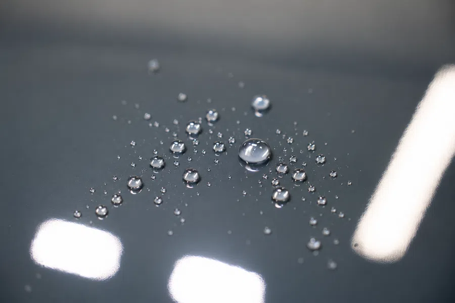 Close-up of numerous water droplets on a smooth dark surface reflecting light bright spots.