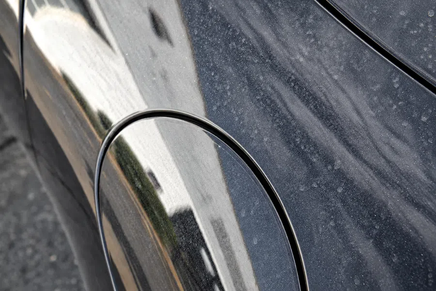 Close-up of a dusty black car's fuel cap area reflecting surroundings on its glossy surface.
