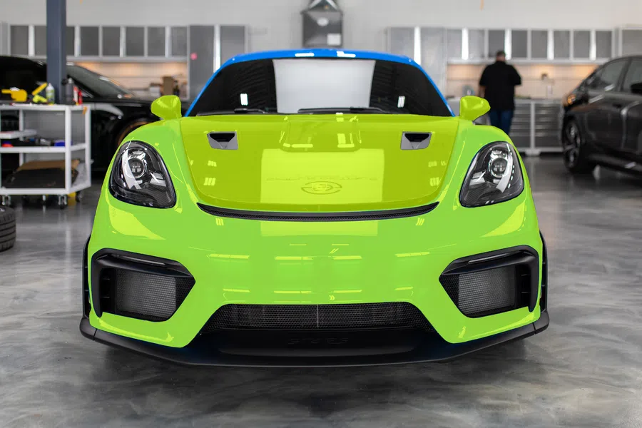 Front view of a lime green sports car with blue roof inside a garage with other vehicles.