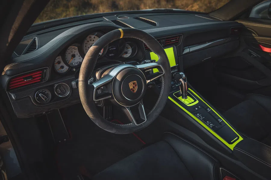 Porsche car interior with black steering wheel, dashboard, and neon yellow accents on center console and display.