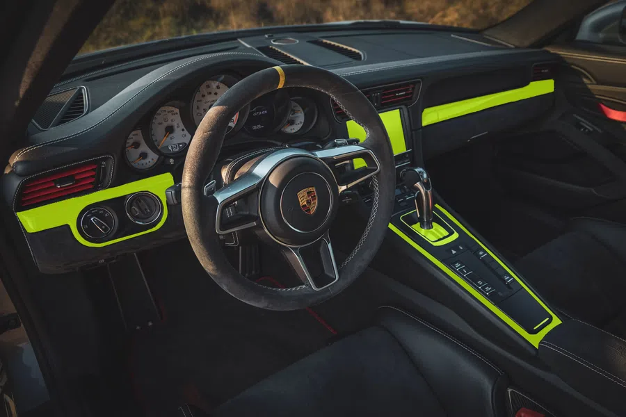 Porsche car interior with black leather steering wheel, dashboard, and neon yellow trim accents.