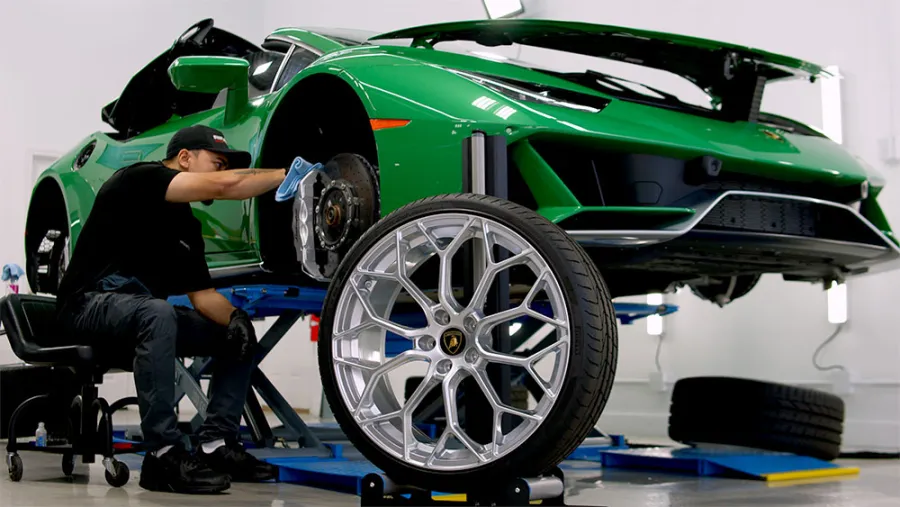 Mechanic working on a green sports car with the front wheel removed in a modern workshop.