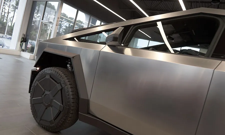 Close-up of a metallic silver Tesla Cybertruck's side panel and rear wheel in a showroom with large windows.