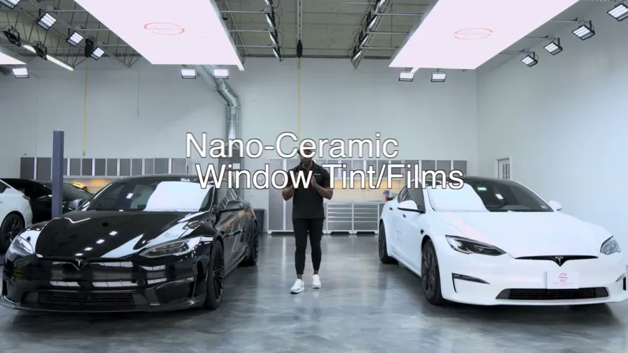 Black and white Tesla cars side by side in a showroom with a person showcasing nano-ceramic window tint films.