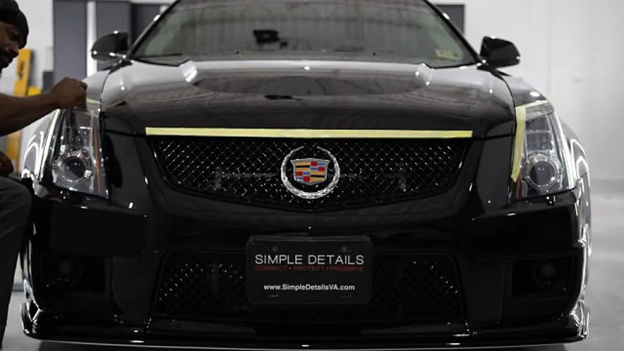 Black Cadillac CTS being detailed, focusing on front grille and status emblem with technician working on left headlight.