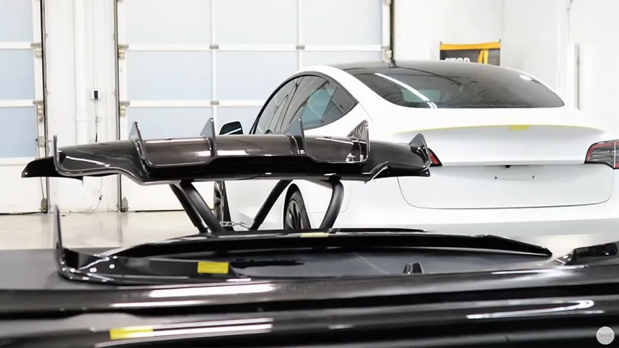 Black car spoiler displayed in front of a white sedan inside a bright garage with step doors.