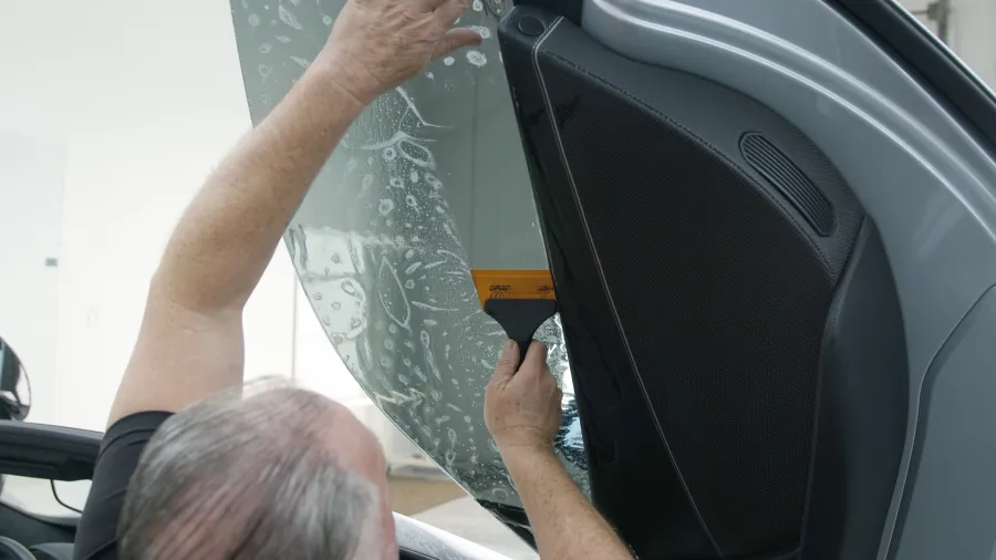 Technician applying window tint film to a car door using a squeegee tool for smooth installation.
