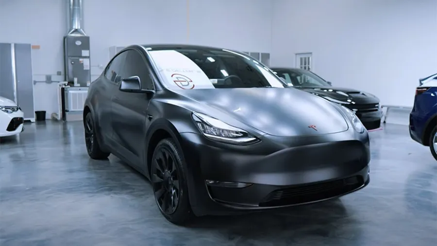 Matte black Tesla Model Y electric SUV parked indoors with sleek design and modern headlights.