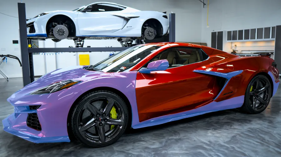 Two Chevrolet Corvette sports cars in a workshop, one custom purple and red in foreground, white on lift in background.