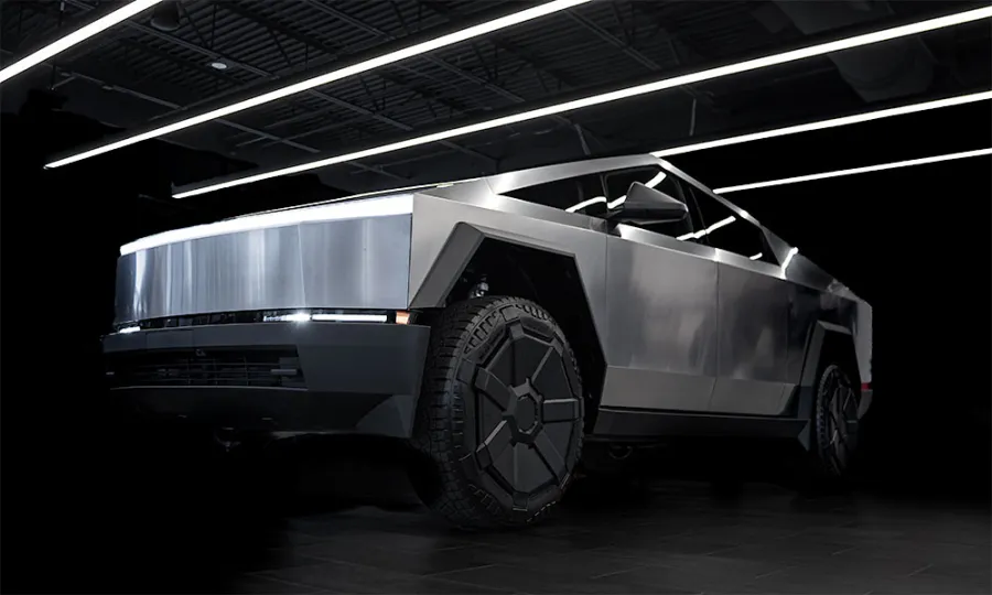 Futuristic silver electric pickup truck with angular design and large tires under bright linear ceiling lights.