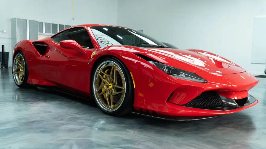 Shiny red Ferrari sports car with gold rims parked on glossy showroom floor indoors