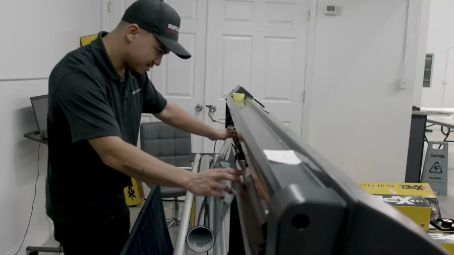 Technician adjusting large commercial printer in a workshop with various printing materials around.