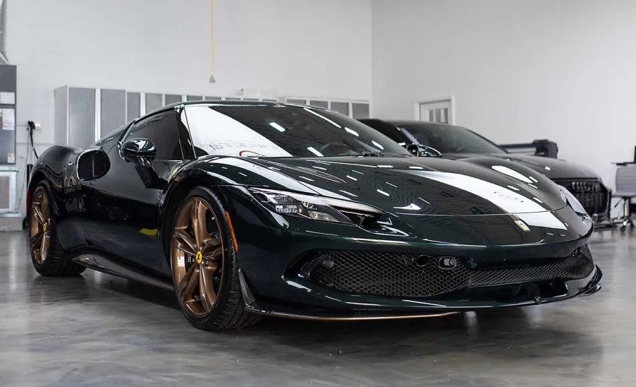 Black luxury Ferrari sports car with bronze wheels parked indoors on a polished concrete floor under bright lighting.