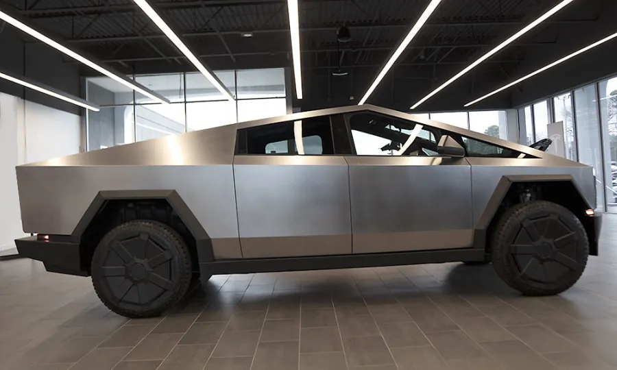 Side view of a metallic silver Tesla Cybertruck showcased in a modern showroom with tiled floor and overhead lighting.