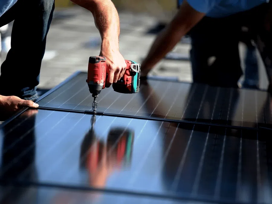 Worker using a drill to install solar panels on a rooftop under sunny conditions