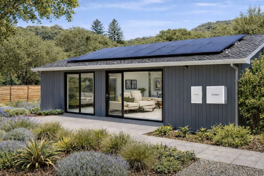 Modern gray house with solar panels on the roof and landscaped garden under a blue sky.