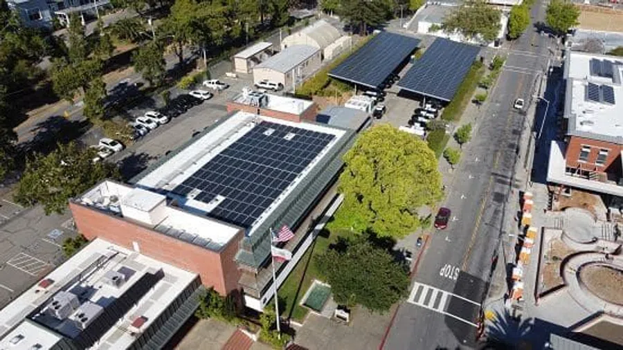 Aerial view of a building with solar panels on the roof and parking canopies surrounded by trees and streets.