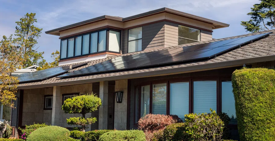 Modern house with solar panels on the roof surrounded by green shrubs and trees under a clear sky