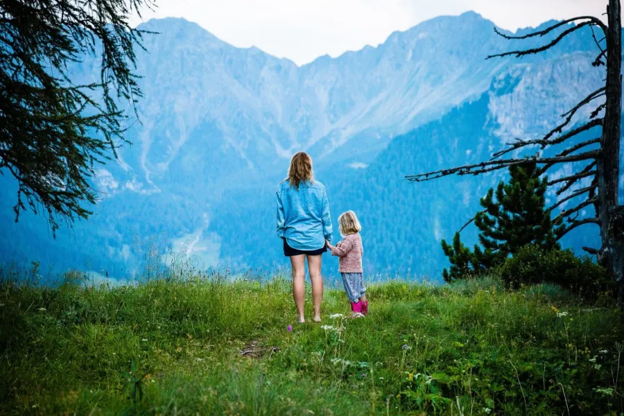 a person and a child walking on a grassy hill with mountains in the background