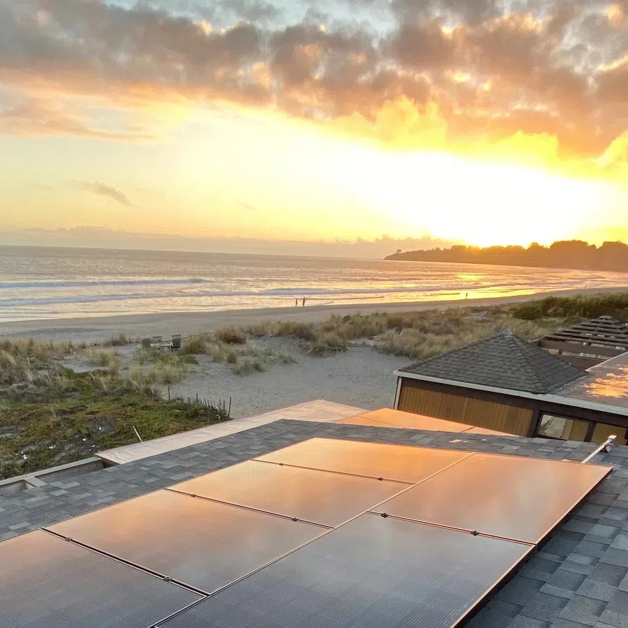 Rooftop solar panels reflecting sunset light with beach, ocean, and cloudy sky in the background
