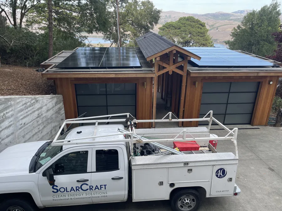 White SolarCraft service truck parked outside a modern home with solar panels on the roof surrounded by trees and hills.