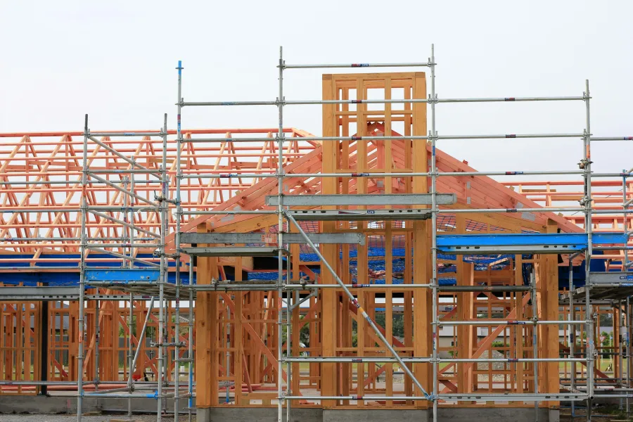 Wooden house framework under construction with scaffolding and clear sky background.