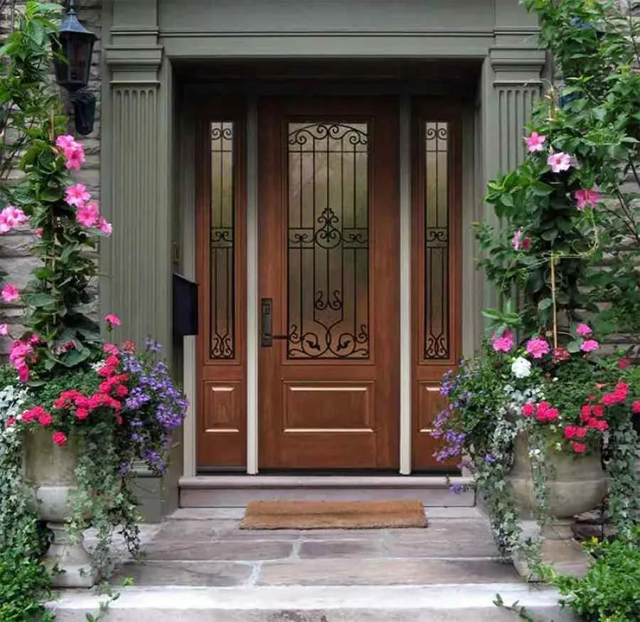 Wooden front door with decorative glass panels surrounded by blooming pink and purple flowers in large stone pots.