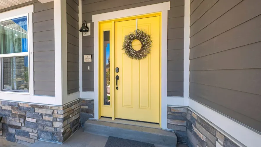 Exterior of a home with gray siding and stone facade, showcasing a bright yellow front door with a decorative wreath.