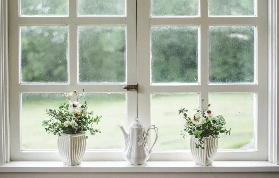 a couple of white vases with flowers in them by a window