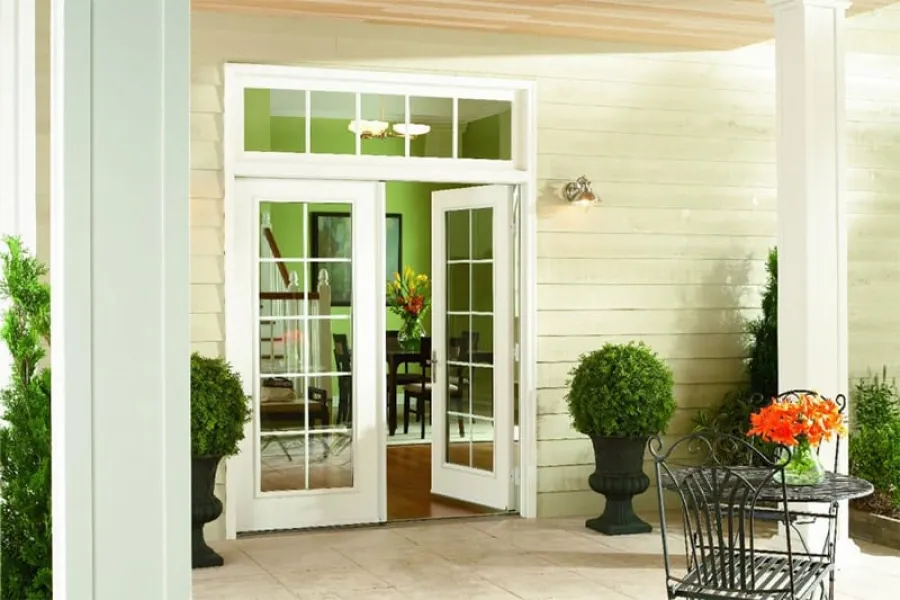 Cozy patio with open white French doors leading to a bright green interior dining area with floral centerpiece