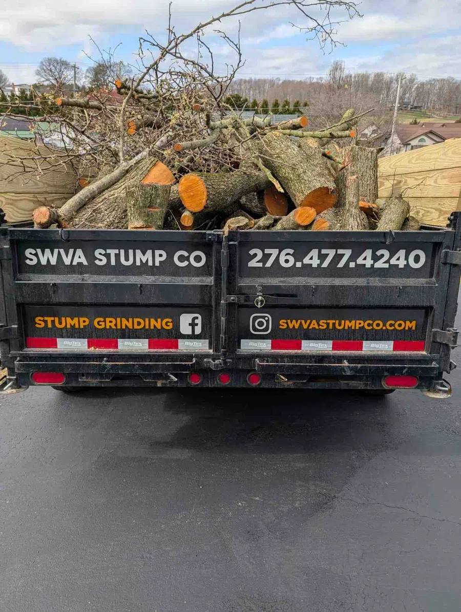 Trailer loaded with cut tree branches and logs from SWVA Stump Co offering stump grinding services.