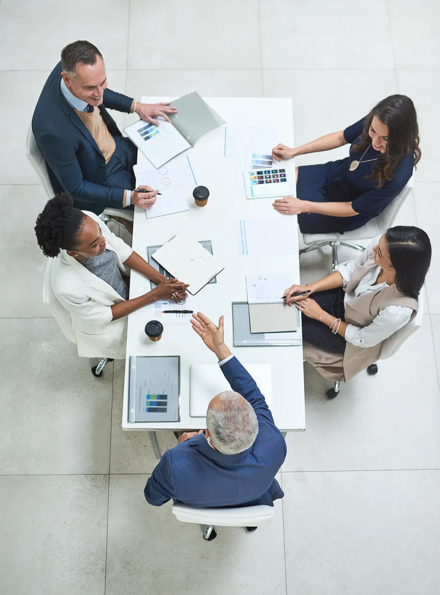Top view of diverse business team having a meeting around a white table with documents and coffee cups.