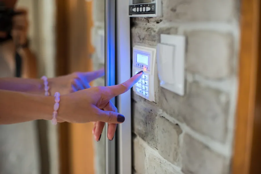 Person entering code on a security keypad mounted on a stone wall near a glass door for access control.
