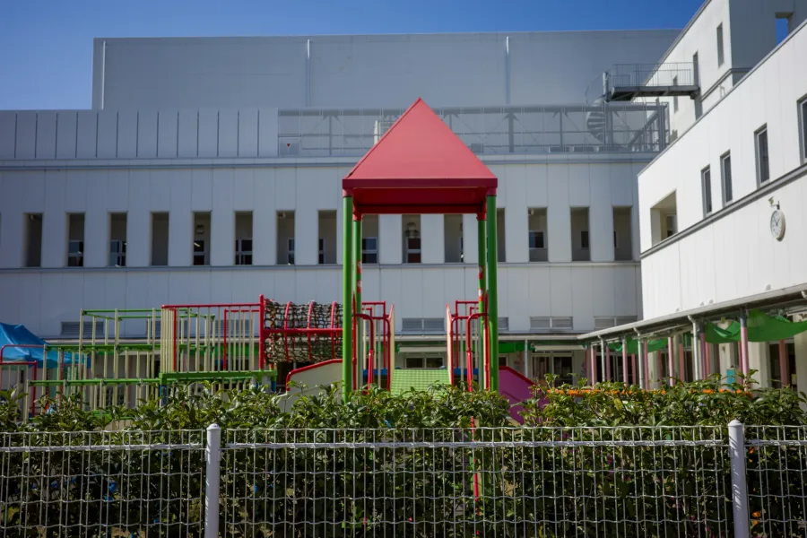 Colorful playground with slides and climbing structures in front of a modern school building under clear blue sky