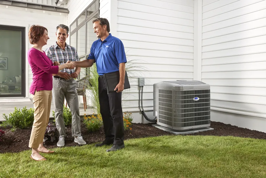 Homeowner shaking hands with HVAC technician near air conditioning unit outside house on lawn