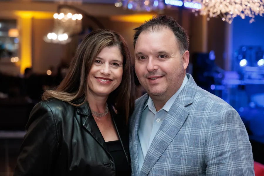 Smiling man and woman in formal attire at an indoor event with warm lighting and chandelier in the background