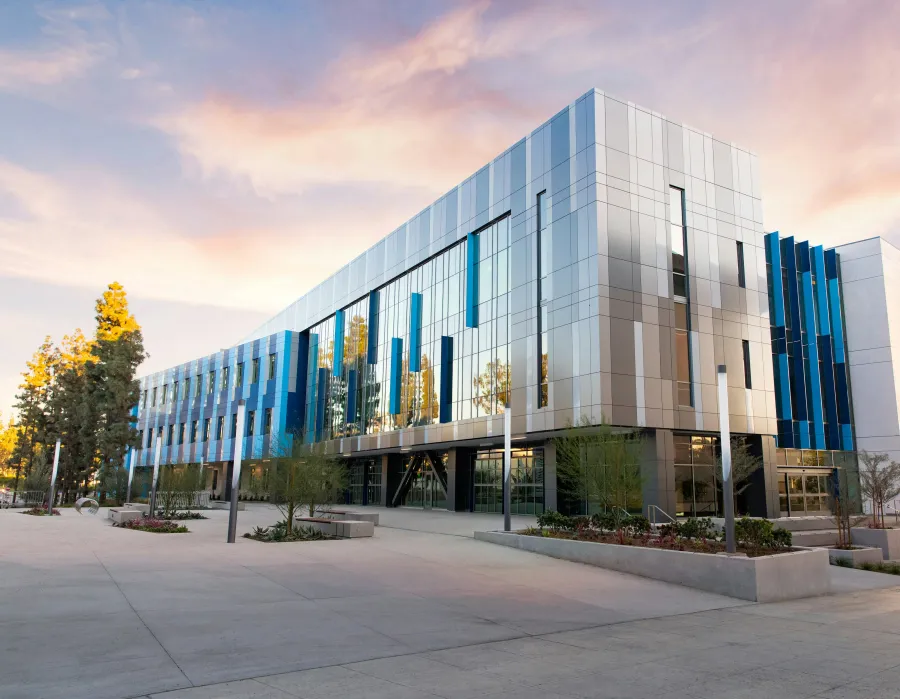 Modern glass and metal office building with landscaped surroundings under a colorful evening sky.