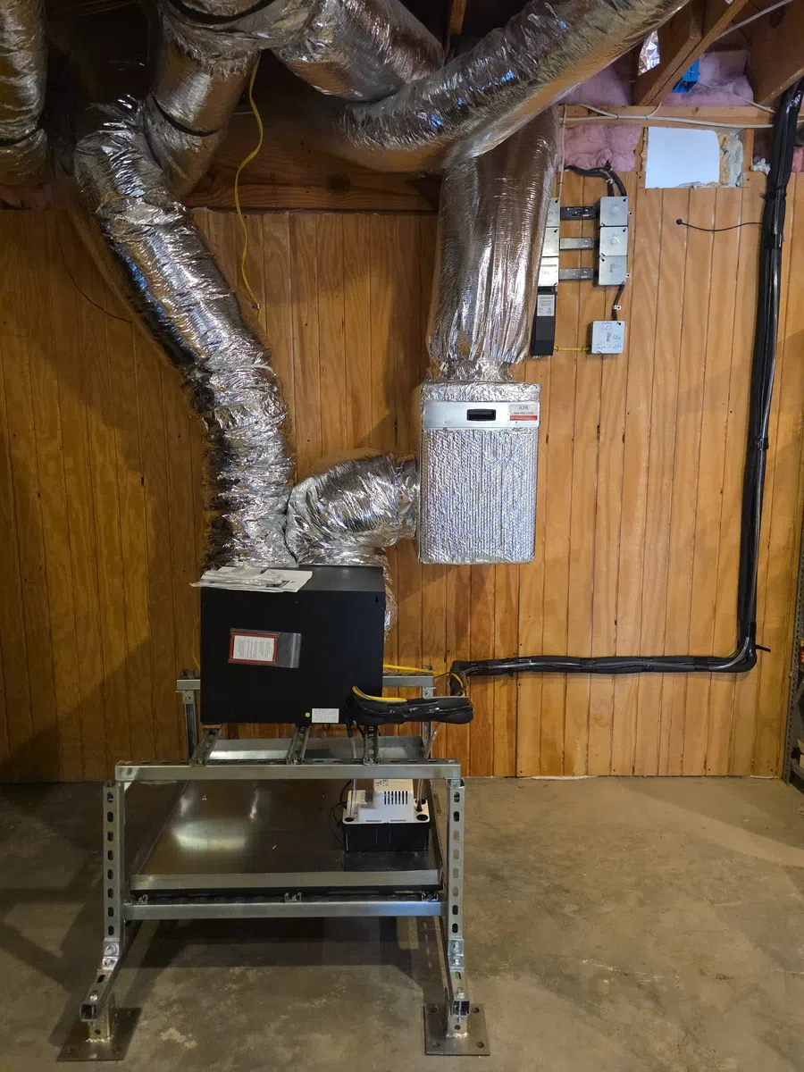 Indoor HVAC unit with insulated ducts and metal stand against wooden panel wall in basement setting.
