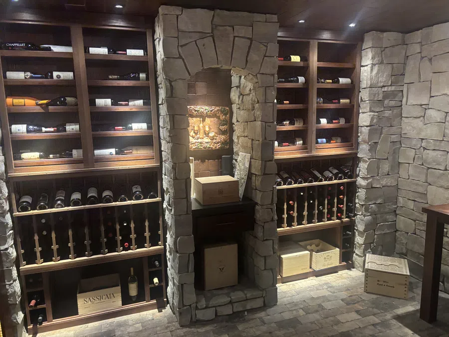 Wine cellar with stone walls, wooden racks filled with wine bottles and wooden wine crates on stone floor.