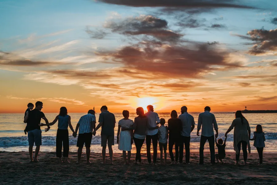 a group of people standing on a beach looking at the sunset