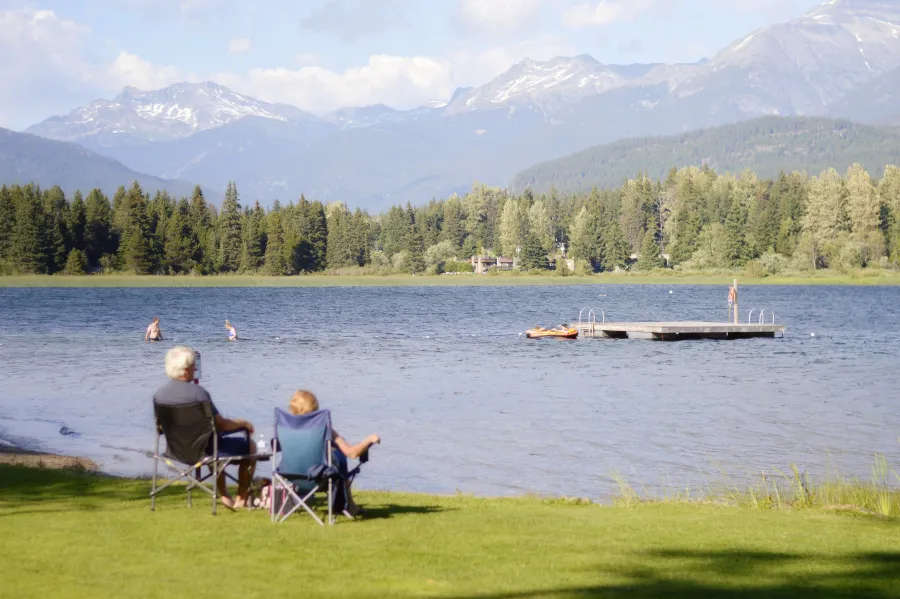 a group of people sitting in chairs on a grassy field by a lake