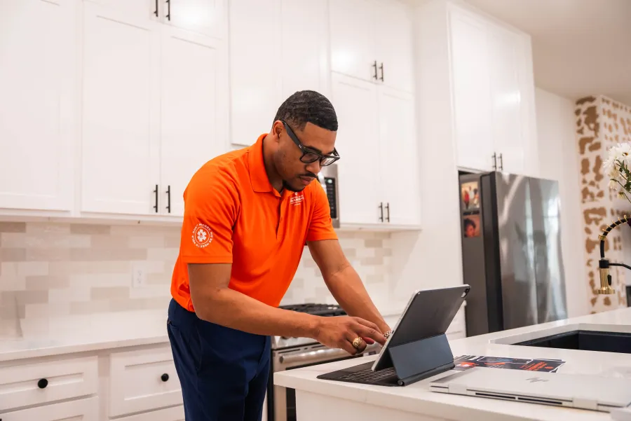 Three people discussing and reviewing information on a tablet in a modern kitchen setting with tools on the counter