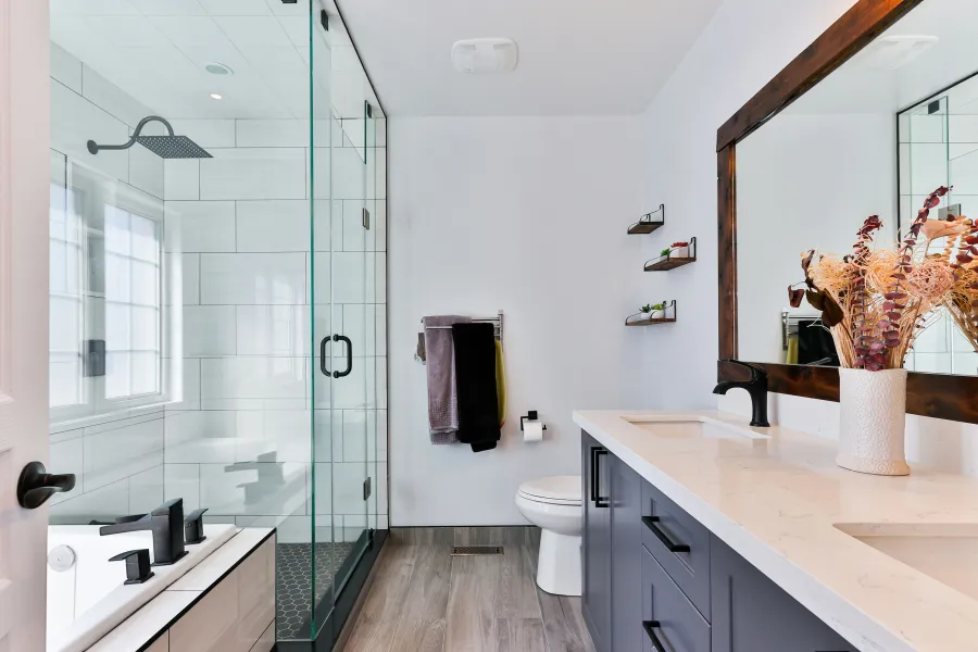 Modern bathroom featuring a glass shower, stylish mirror, and decorative vase with dried flowers.