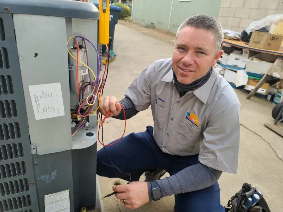 Technician in yellow shirt servicing an Innovair HVAC unit outdoors with diagnostic tools connected.
