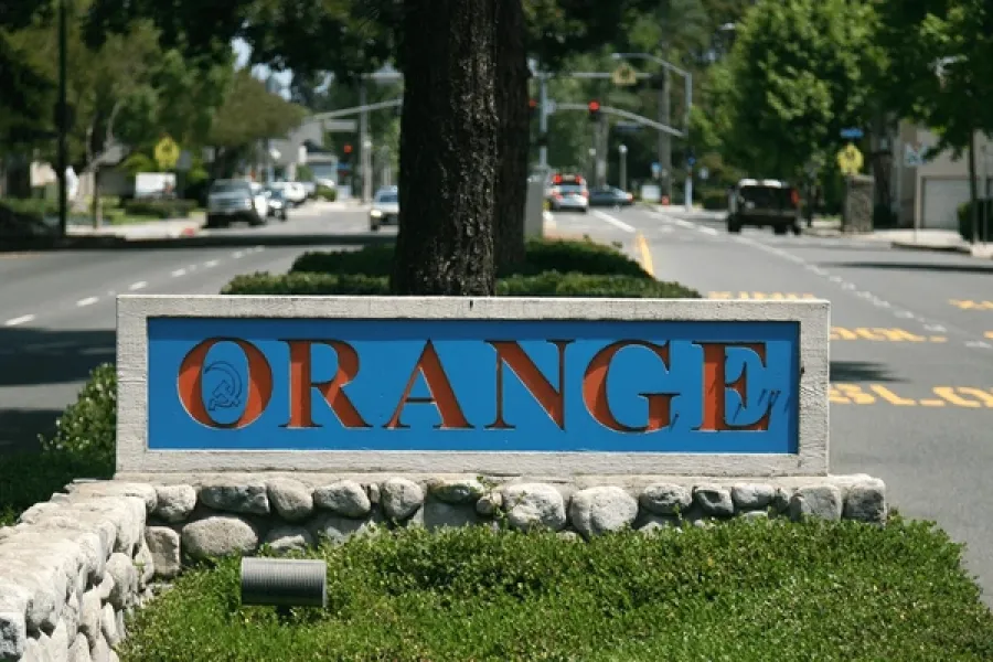 Street view of Orange city, CA sign with stone base and greenery on a sunny day